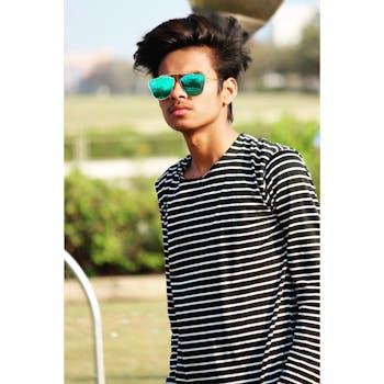 一名年轻人戴着墨镜、穿着条纹衬衫，在户外公园自信地摆姿势