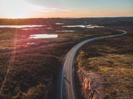 A winding road surrounded by wetlands and fields at sunset, captured from above.