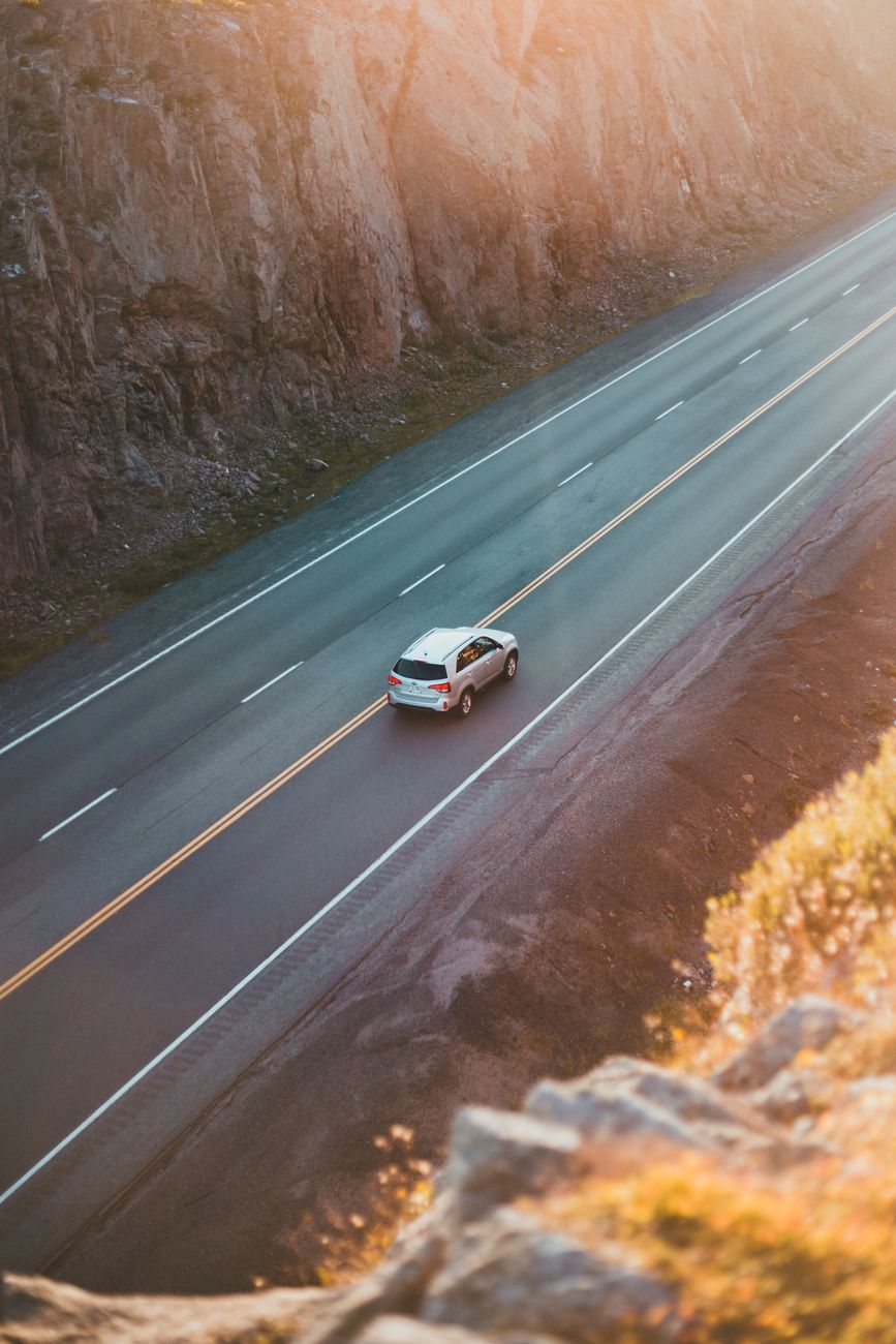 cinematic aerial view of a winding desert road at golden hour with a black sports car