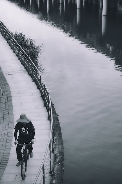 Grayscale Photo of a Person Riding a Bicycle by the River