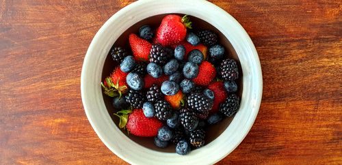 Free A vibrant assortment of strawberries, blackberries, and blueberries in a bowl on a wooden surface. Stock Photo
