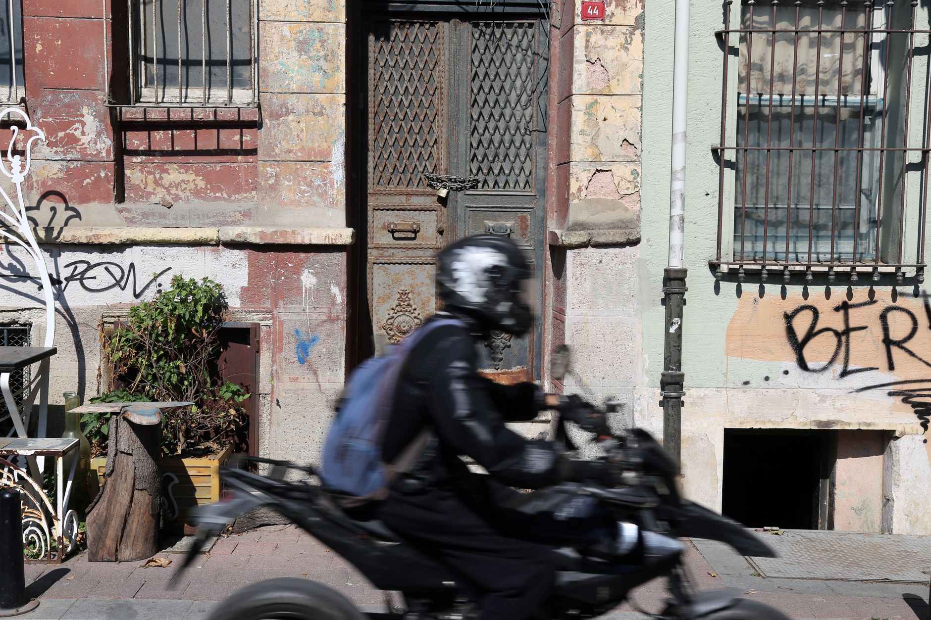 Motorcyclist riding past a weathered building with graffiti art, capturing urban decay and movement.