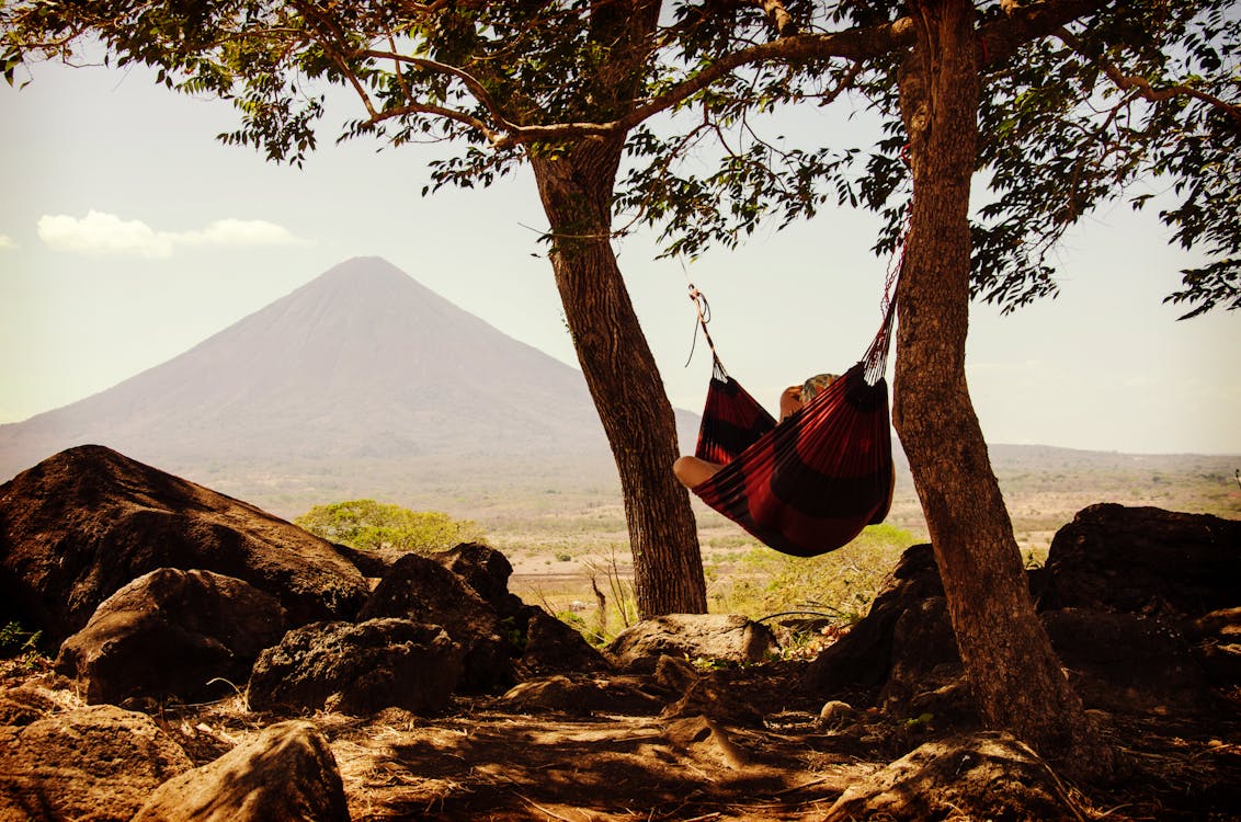 Free Person Lying on Black and Red Hammock Beside Mountain Under White Cloudy Sky during Daytime Stock Photo