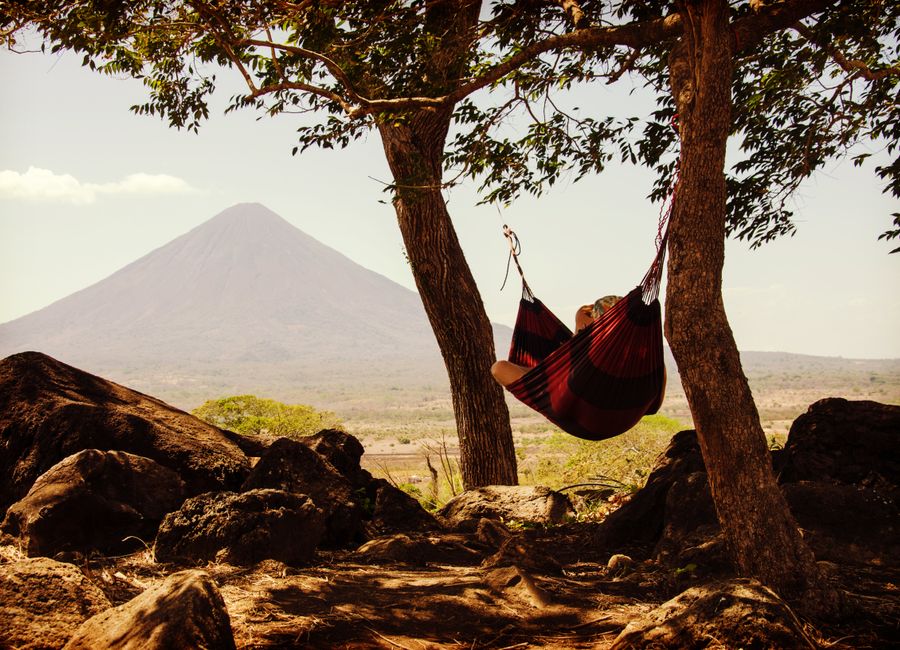 Person relaxing in a hammock between trees with a volcano in the background, capturing tranquility and nature.