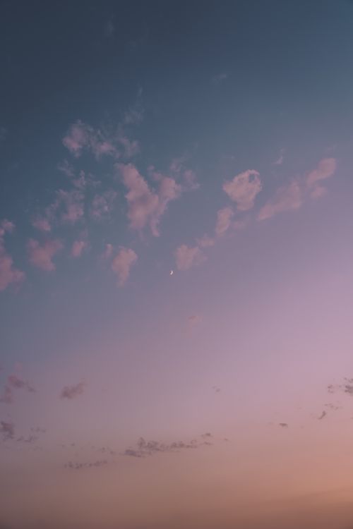 Free A serene view of a pastel-colored sky at sunset featuring scattered clouds and a crescent moon. Stock Photo