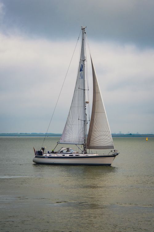 Free A solitary sailboat gracefully cruises on a calm sea under cloudy skies. Stock Photo