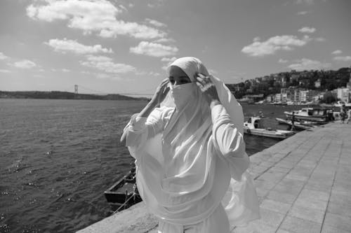 Grayscale Photo of a Woman Wearing Hijab Standing on Seaside