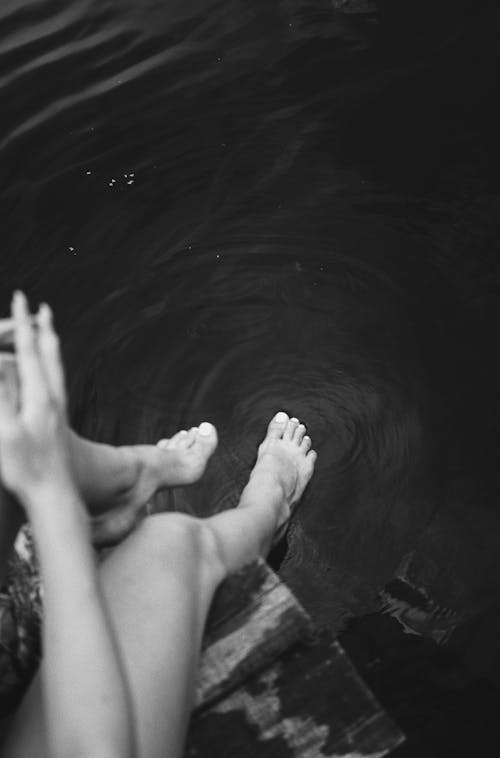Grayscale Photo of Persons Feet on Water