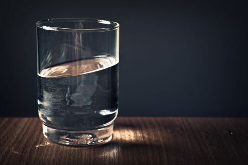 Free A clear glass of water sitting on a wooden table against a dark background. Stock Photo