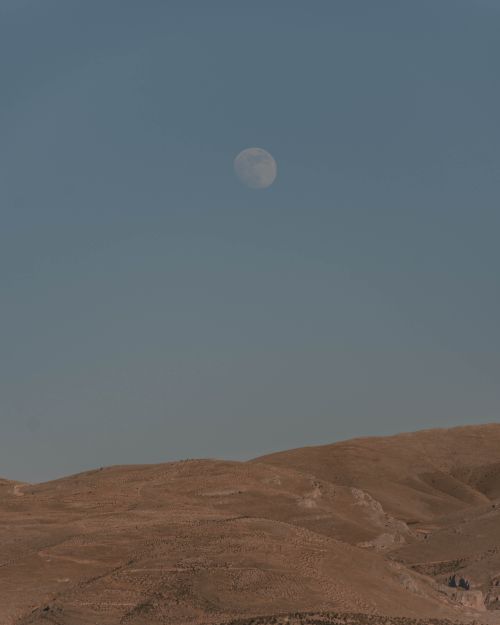 Free A serene desert landscape with rolling hills under a blue sky and visible moon at dusk. Stock Photo