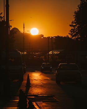 Urban street scene during sunset with cars silhouetted against the sun, showcasing vibrant urban life.