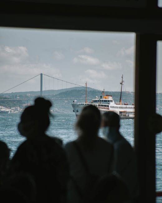 Silhouette of people on a ferry with a bridge in the distant background over calm waters.