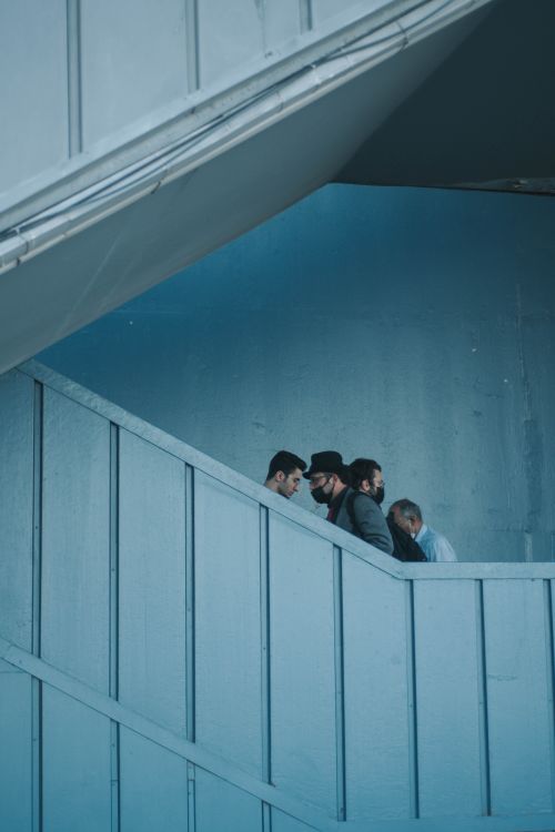 Free Four adults ascending a blue-painted stairway indoors, suggesting contemporary fashion and lifestyle. Stock Photo