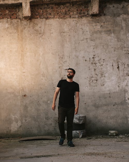 Man in Black Crew Neck Shirt and Pants Standing Beside the Concrete Wall
