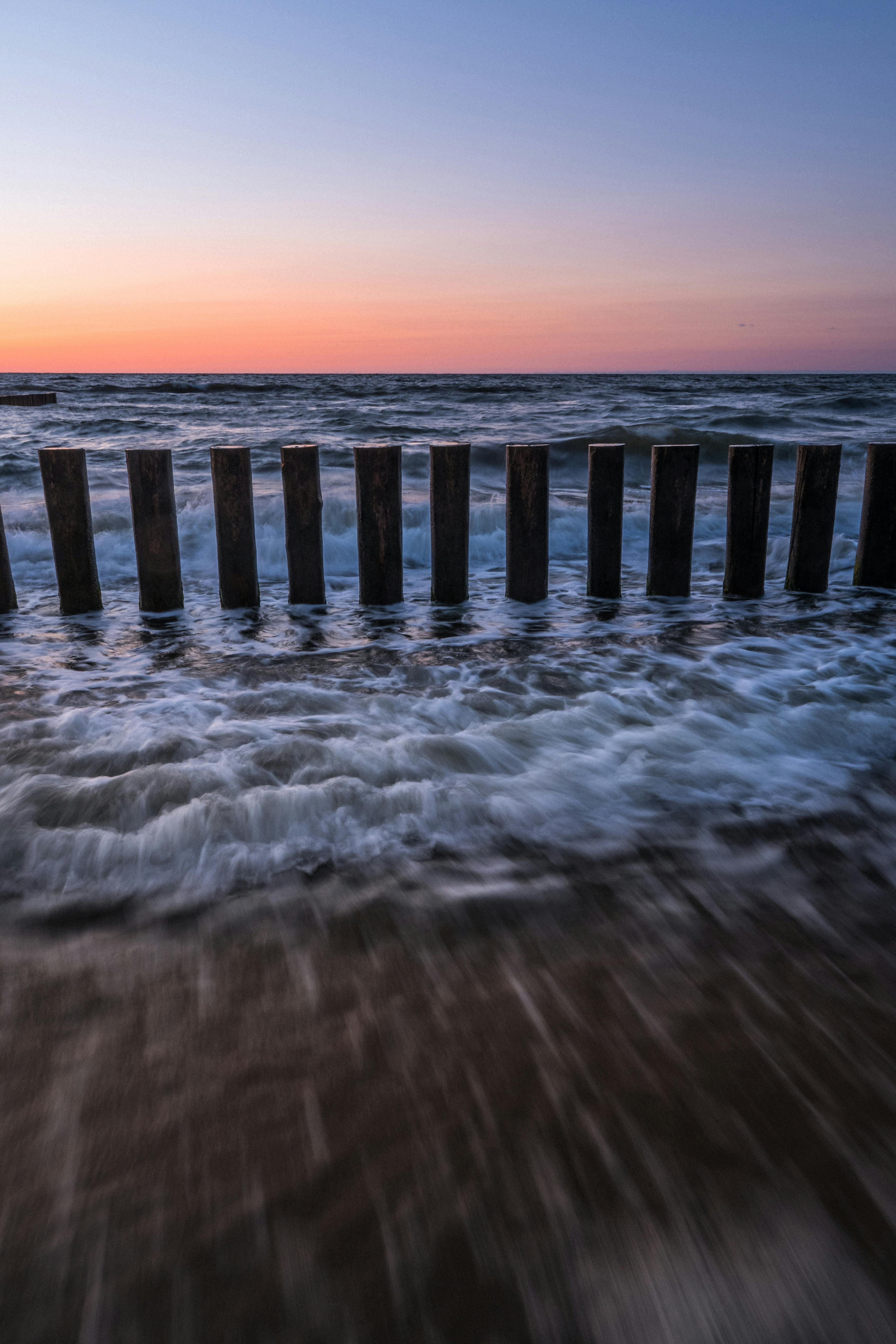 Dramatic seascape with waves crashing against wooden breakwater at sunset, ideal for coastal themes.