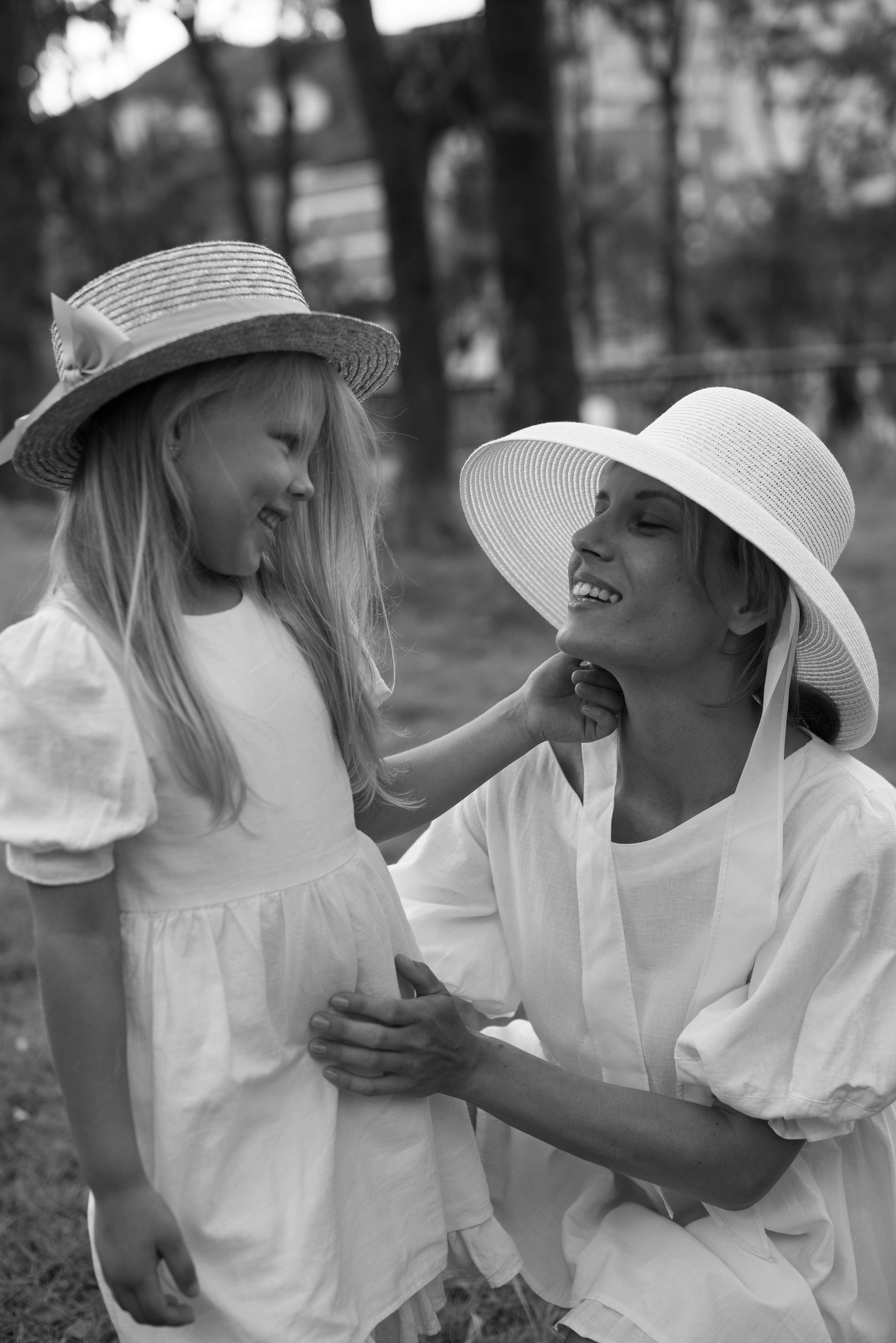 Black and white photo of a joyful mother and daughter in sun hats sharing a moment outdoors.