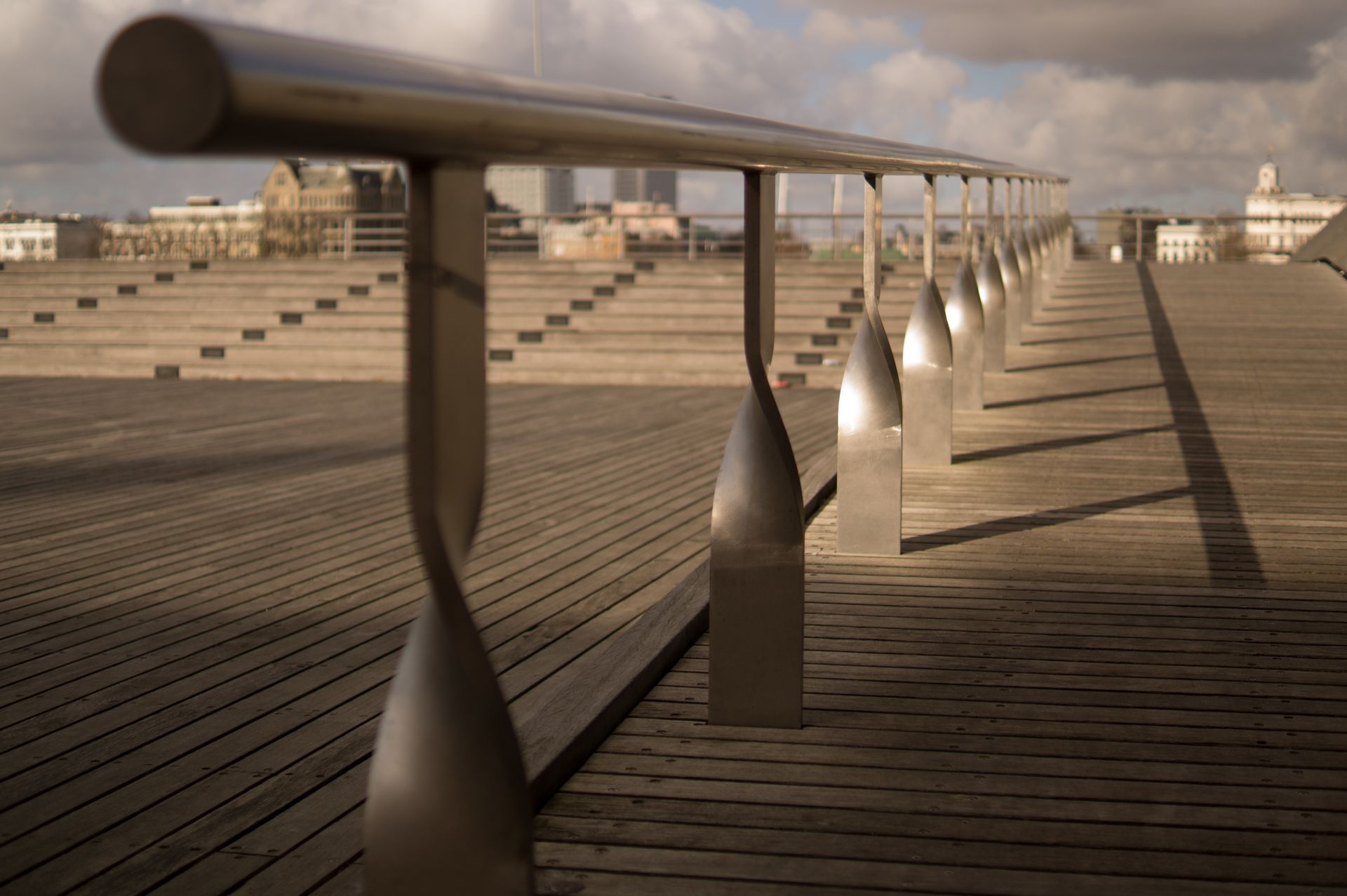 A modern urban scene featuring a wooden deck and sleek metal railings with a cityscape in the background.