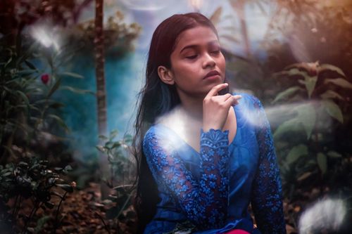 Free A tranquil portrait of a woman in a blue dress surrounded by forest plants and soft lights. Stock Photo
