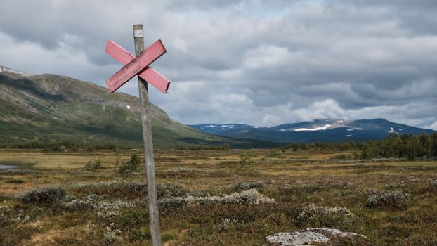 Wooden signpost in a meadow with hills and cloudy sky.