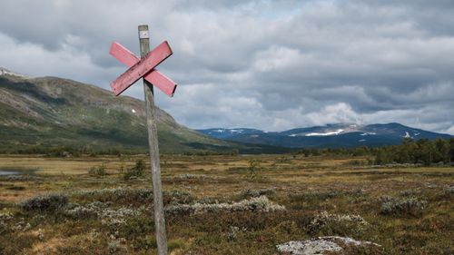 Free Wooden signpost in a meadow with hills and cloudy sky. Stock Photo