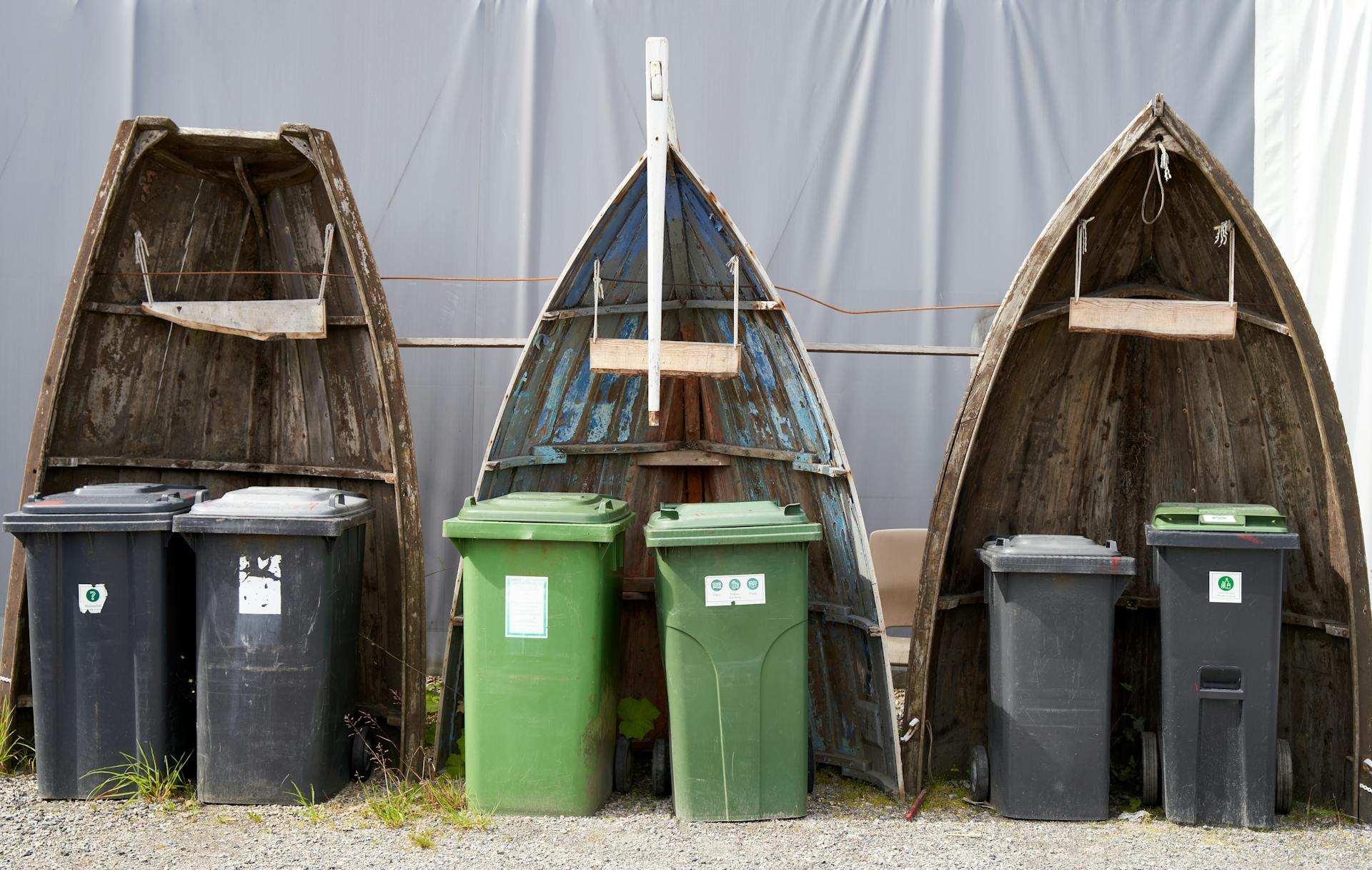 Recycling bins placed within upcycled boat hulls create an artistic outdoor installation.