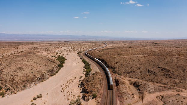 Expansive desert view with a lone train track curving through arid terrain under a clear sky.