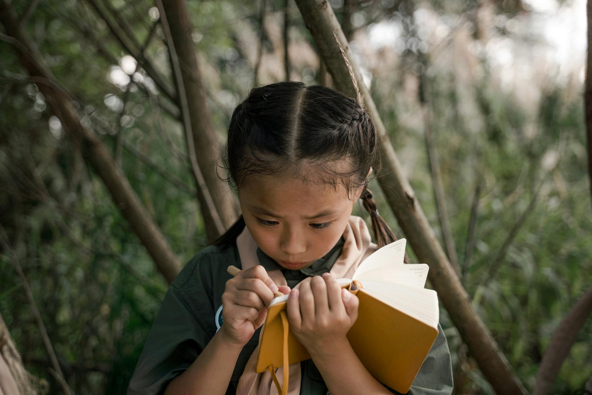 Young girl scout in forest taking notes in a notebook.