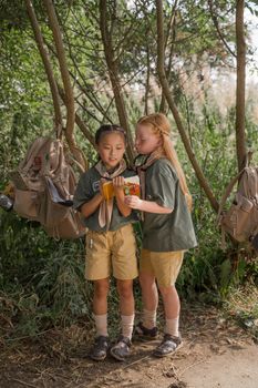 Two young scouts taking notes in a forest setting, surrounded by nature.