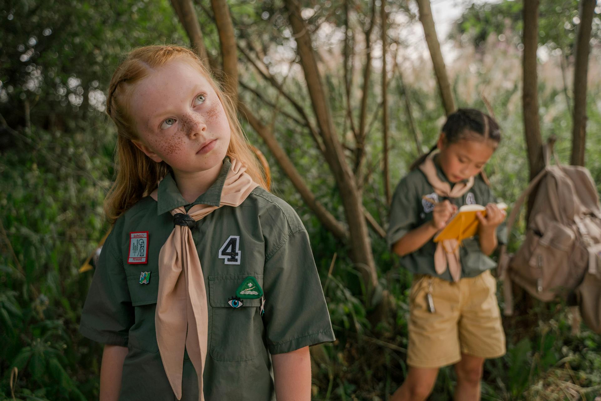 Two girl scouts in uniform explore nature, learning and taking notes.