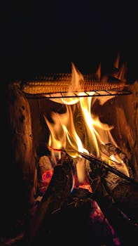 Roasted corn grilling over an open flame on a traditional stove during a dark night.
