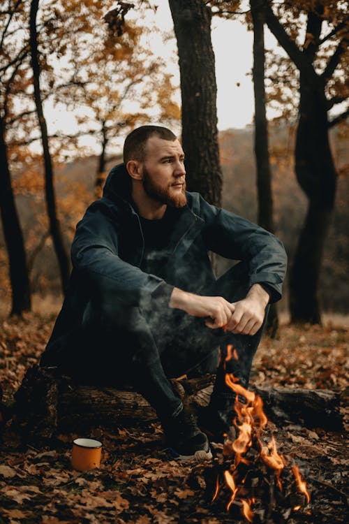 Man in Black Leather Jacket Sitting on Tree Log