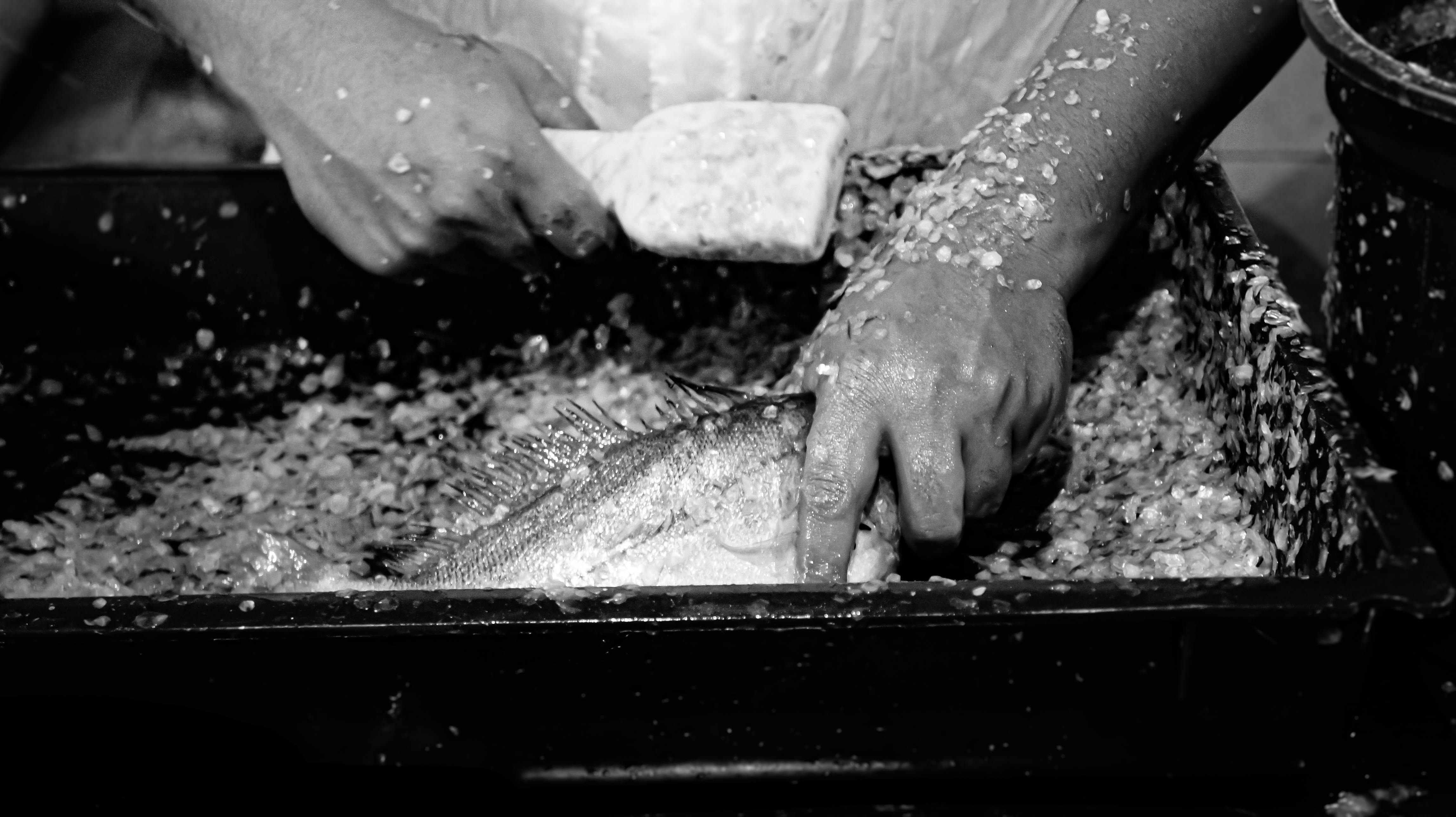 Hands scaling a fish in a black and white Brazilian market setting, showcasing a traditional process.