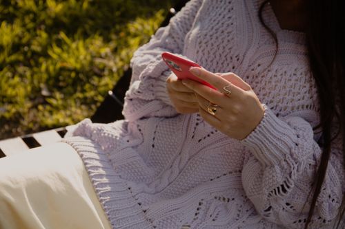 Free Close-up of a woman in a knitted sweater using a smartphone while relaxing outdoors. Stock Photo