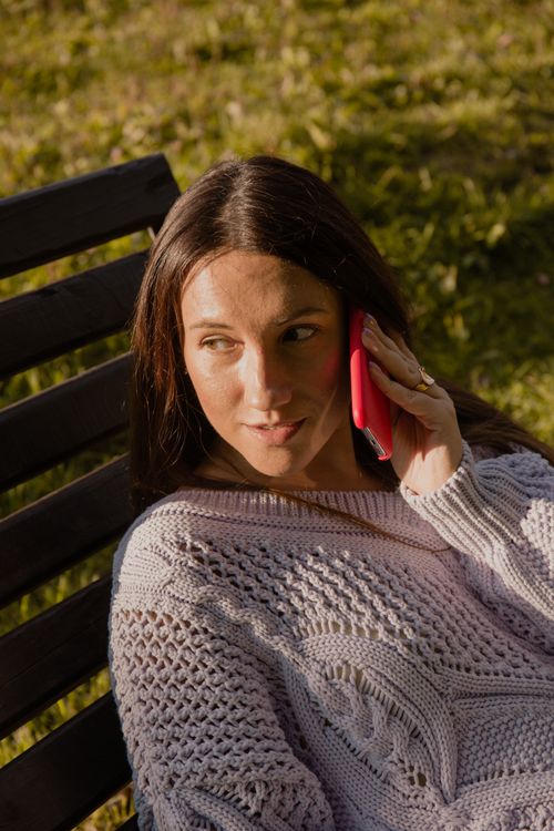 Free Woman sitting on a bench outdoors, holding a cellphone and enjoying sunlight. Stock Photo