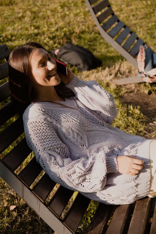 Free A young woman enjoys a phone call while lounging on a park bench outdoors. Stock Photo