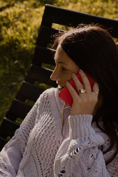 Brunette woman outdoors on phone, wearing casual sweater, side view.