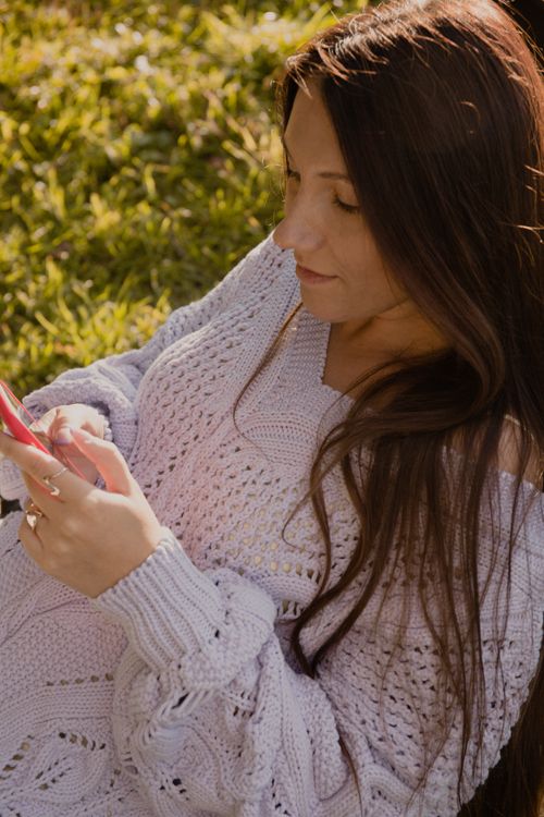 Free A woman in a cozy knitted sweater browses her smartphone while enjoying the outdoors. Stock Photo