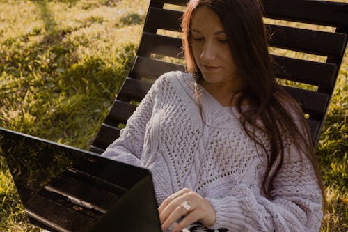 Free Woman in Knitted Wear Sitting on Wooden Chair Using Laptop Stock Photo
