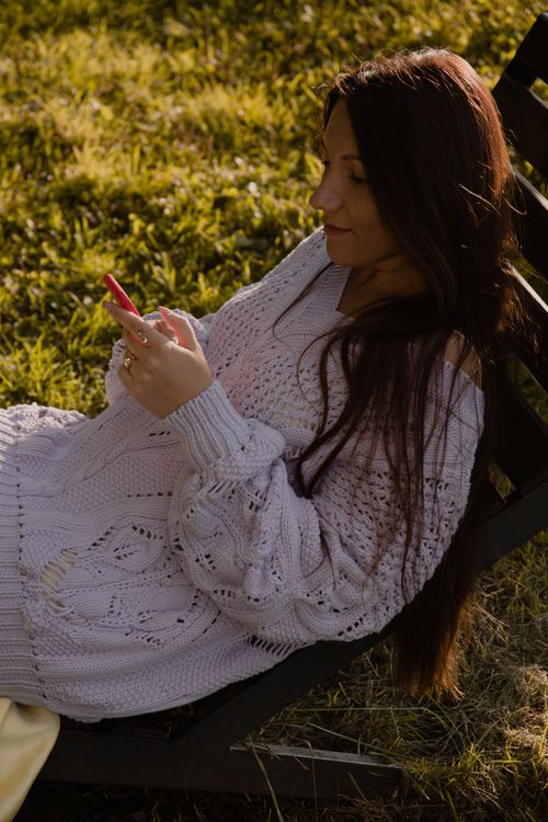Free Woman in a cozy knitted sweater using her smartphone outdoors on a sunny day. Stock Photo