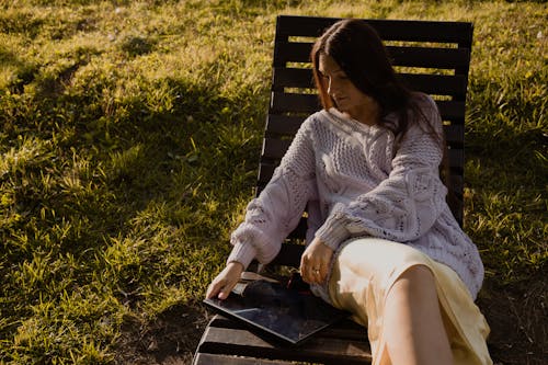 Free Woman in White Knit Sweater Sitting on Wooden Chair with a Laptop Stock Photo
