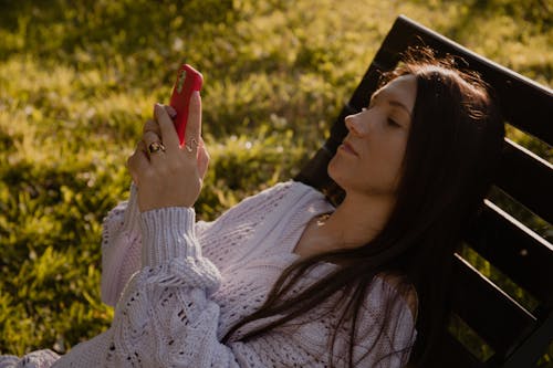 Free Woman in White Knit Sweater Using a Red Smartphone Stock Photo
