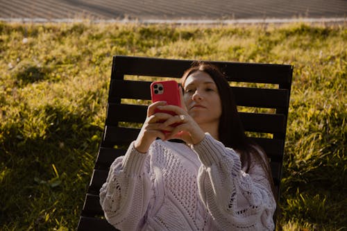 Woman in White Knit Sweater Holding Red Smartphone