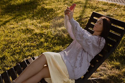 Free Woman Taking Selfie while Lying Down on a Wooden Beach Chair Stock Photo