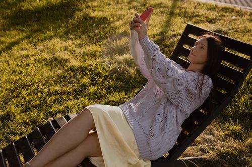 Free A woman relaxes on a chair outdoors capturing a selfie with her smartphone. Stock Photo