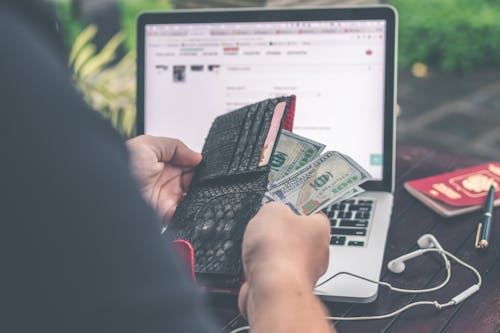 Person Holding 10 Us Dollar Banknote in Front of Gray and Black Laptop Computer