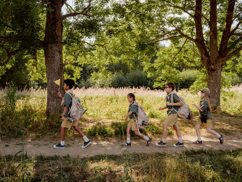 Group of young scouts trekking through a sunny forest trail with backpacks and uniforms - scout history badges and hikes