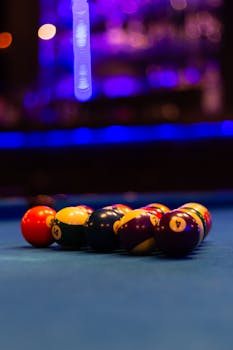 Colorful billiard balls arranged on a pool table in a dimly lit bar setting.