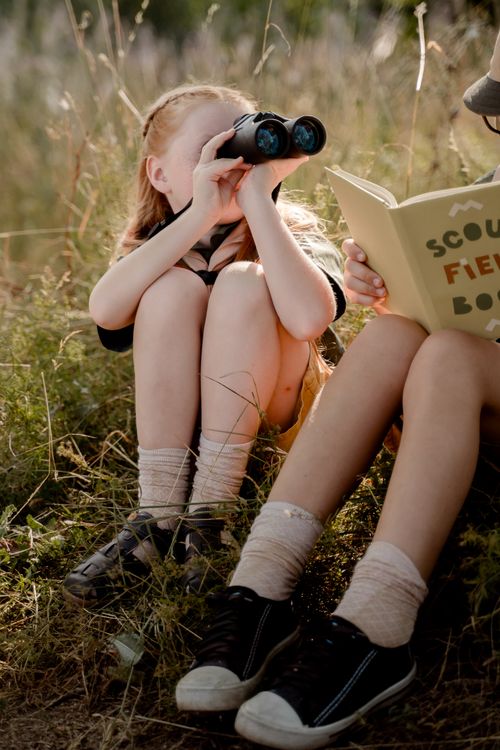 Free Girls explore outdoors with binoculars and a field guide, embracing nature. Stock Photo