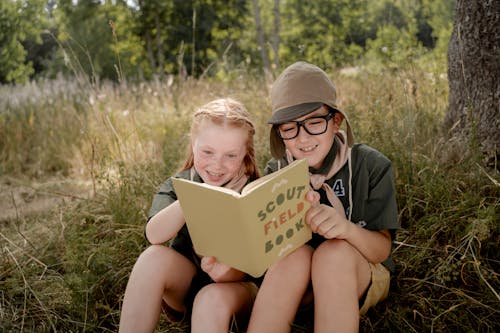 Boy and a Girl Reading a Book while Sitting on the Ground