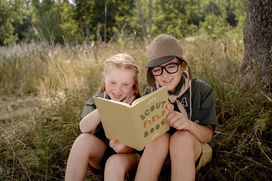 Boy and a Girl Reading a Book while Sitting on the Ground
